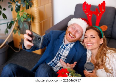 High angle view of cheerful young business people having fun celebrating Christmas at the office, wearing Santa hat and costume reindeer antlers taking selfies using smart phone - Powered by Shutterstock