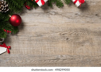 High Angle View Of Christmas Ornaments On Wooden Table With Copyspace. Top View Of Xmas Fir Branch With White Gift Boxes And Red Ball. Rustic Christmas Corner Background.