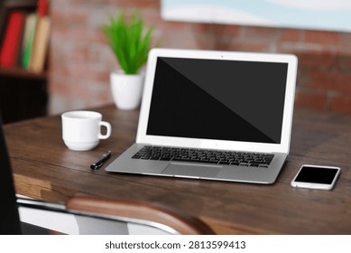 A high angle view of a clean workspace featuring a silver laptop with a blank screen, a white coffee mug, and a smartphone on a dark rustic wooden table.
