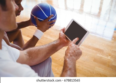 High angle view of coach showing digital tablet to basketball player while sitting on bench in court - Powered by Shutterstock