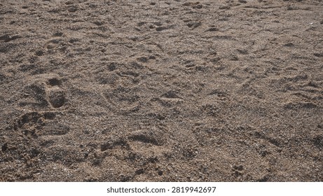 A high angle view of coarse brown beach sand featuring scattered human footprints and natural textures in an outdoor setting.
