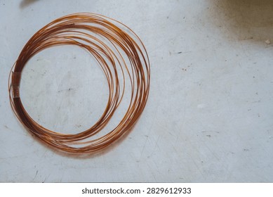 High angle view of a coil of thin brown nylon wire resting on a scratched white workbench.