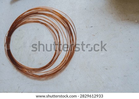 High angle view of a coil of thin brown nylon wire resting on a scratched white workbench.
