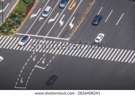 A high angle view of a commercial district intersection with flower planted medians presents flowering median beds separating opposing traffic streams. Far above a crowded downtown district.