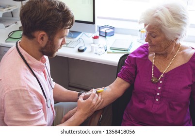 High angle view of confident Caucasian male doctor giving an injection to senior female patient in clinic - Powered by Shutterstock