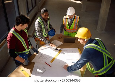 High angle view of construction workers cooperating while working on housing plans at building site. 