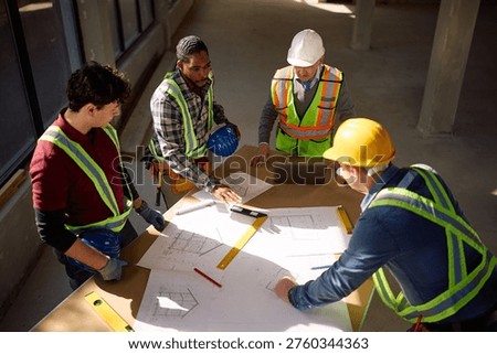 High angle view of construction workers cooperating while working on housing plans at building site. 