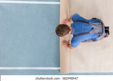 High Angle View Of Craftsman In Overalls Unrolling Carpet On Floor
