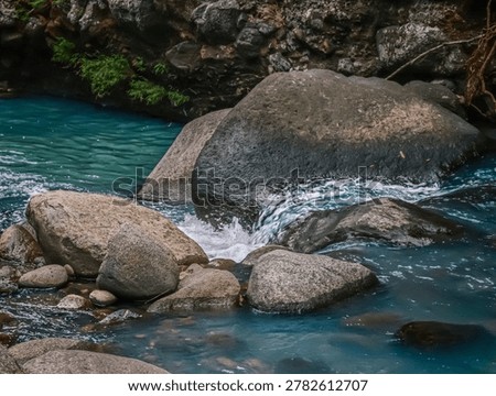 High angle view of crystal clear blue water splashing and flowing between smooth river stones and large boulders, capturing the dynamic movement of a mountain stream in the forest.