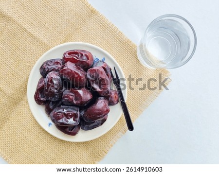 High angle view of dates in a small white plate and a glass of water on a white background. 