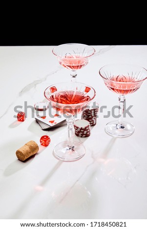 high angle view of deck of cards, glasses of cocktail, dice, casino tokens and cork on white surface isolated on black
