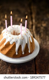 High angle view of a delicious freshly baked vanilla birthday cake glazed with dripping white icing sugar and pearls and decorated with four lit party candles on a rustic wooden table with copyspace