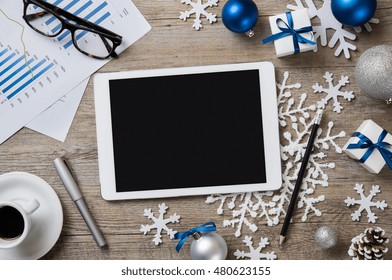 High angle view of digital tablet with black screen on wooden desk with christmas decorations. Top view of digital tablet with business document in a xmas atmosphere with snowflakes.