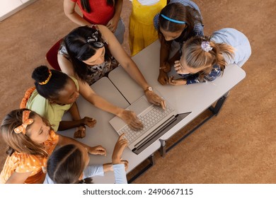 High angle view of diverse female teacher teaching schoolgirls over laptop at desk in classroom. Unaltered, education, student, german, school, childhood, together, e-learning, technology concept. - Powered by Shutterstock