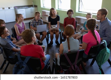 High angle view of a diverse group of elementary school kids sitting on chairs in a circle and interacting during a lesson, their Caucasian male teacher sitting with them and talking