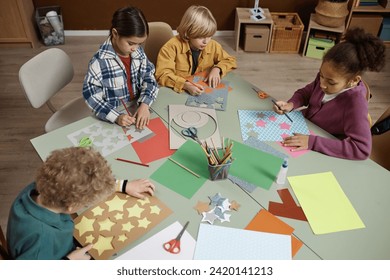 High angle view at diverse group of young children enjoying art and craft class at table in school, copy space