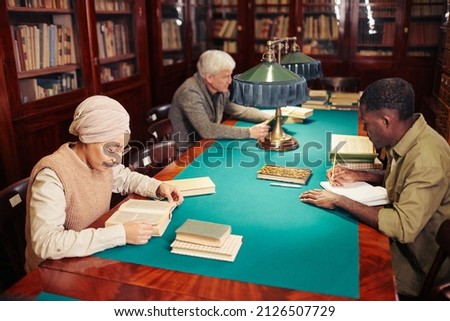 High angle view at diverse group of people studying in library by cozy lamp light