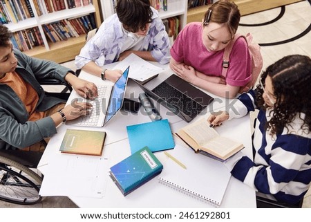 High angle view of diverse group of students sitting at table in school library together and doing research with textbooks and computers copy space