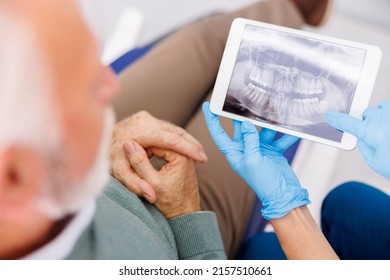 High Angle View Of Doctor Showing Jaw X-ray On Tablet Computer To Patient Sitting At Dental Chair At Dentist Office