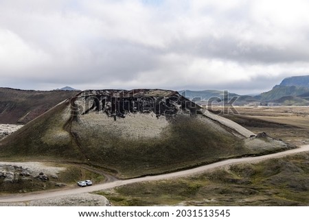 High angle view of a dormant volcano on the volcanic plateau nearby Katla volcano in Iceland with mountains in the background and cars parked at foot of volcano