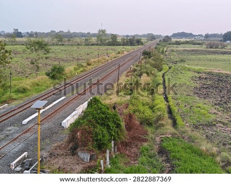 High angle view of a double-track railway stretching into the distance through green rural agricultural fields under a clear sky