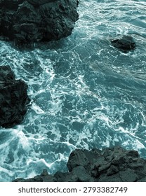 High angle view of dynamic turquoise ocean water crashing against dark volcanic rock formations at Batu Angus Beach in Bitung, North Sulawesi, Indonesia, creating beautiful seafoam textures.