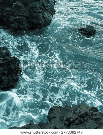 High angle view of dynamic turquoise ocean water crashing against dark volcanic rock formations at Batu Angus Beach in Bitung, North Sulawesi, Indonesia, creating beautiful seafoam textures.