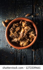high angle view of an earthenware casserole with some pieces of rabbit, prunes and mushrooms, typically eaten in spain, on a gray rustic wooden table