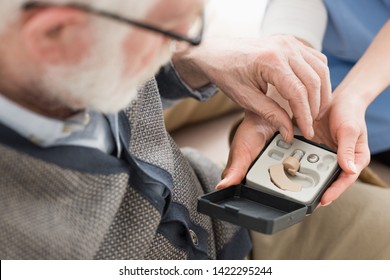 High Angle View Of Elderly Man Looking At Box With Hearing Aid