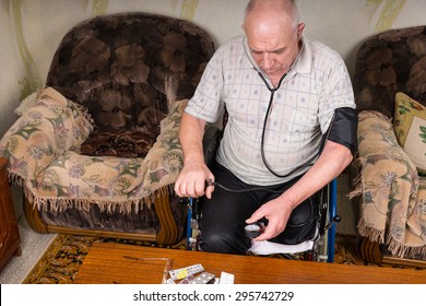 High Angle View Of An Elderly Man With Special Needs Sitting On His Wheelchair, Checking His Blood Pressure Using A Manual BP Apparatus Inside His House.