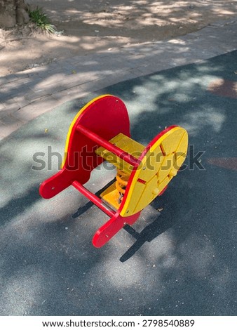High angle view of an empty red and yellow turtle shaped spring rider toy on a green rubber mat at a playground.