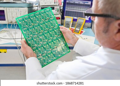 A high angle view of an engineer examining the printed circuit board at an electrical test bench equipped with oscilloscope and multimeters