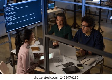 High angle view of ethnically diverse engineers working together on software in IT company office late in evening
