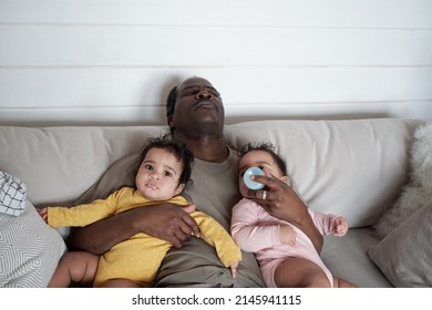 High Angle View Of Exhausted Mature African American Dad Falling Asleep While Taking Care Of His Baby Twin Daughters