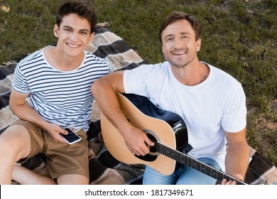 high angle view of father playing acoustic guitar near teenager son with smartphone - Powered by Shutterstock