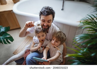 High Angle View Of Father With Two Small Children Brushing Teeth Indoors At Home And Taking Selfie, Sustainable Lifestyle Concept.