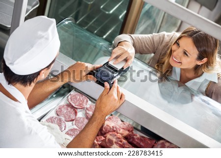 High angle view of female customer paying through smartphone at butchery