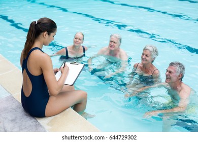 High angle view of female instructor writing while instructing senior swimmers at poolside - Powered by Shutterstock