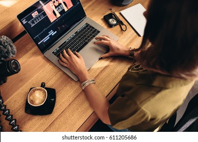 High angle view of female vlogger editing video on laptop. Young woman working on computer with coffee and cameras on table. - Shutterstock ID 611205686