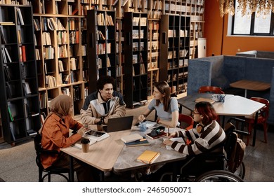 High angle view of four young ethnically diverse gen Z students sitting at table in modern university library preparing for tests