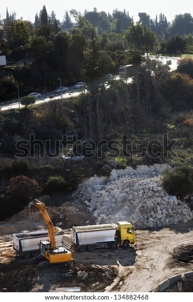 High angle\
view of a front-end loader doing earthworks on a hill, gnawing at\
the hillside and loading the rocks and dirt onto a heavy truck;\
preparing the ground for\
construction.