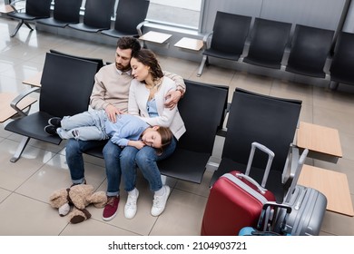 high angle view of girl sleeping on knees of tired parents in airport lounge