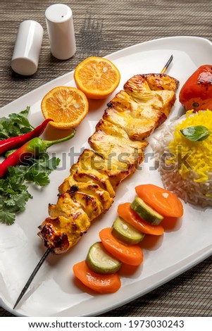 High angle view of grilled chicken kebab on a simple plate. Called Chelo Joojeh in Persian cuisine, as it is served with rice and grilled tomato.Fusion food barbecue concept.