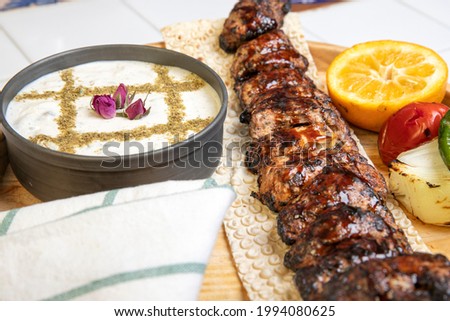 High angle view of grilled chicken kebab on a simple plate. Called Chelo Joojeh in Persian cuisine, as it is served with rice and grilled tomato.Fusion food barbecue concept.