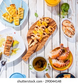 High Angle View Of Grilled Fruit And Seafood Dishes Arranged On White Wooden Table Surface