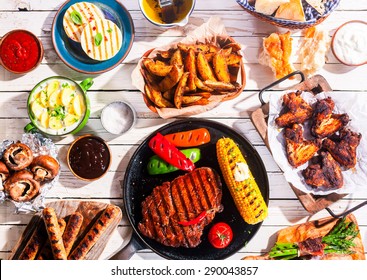 High Angle View of Grilled Meal - Appetizing Barbequed Meats and Vegetables Arranged on White Wooden Picnic Table
