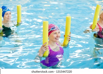 High angle view at group of active senior women exercising in swimming pool, holding pool noodles and smiling, copy space - Powered by Shutterstock