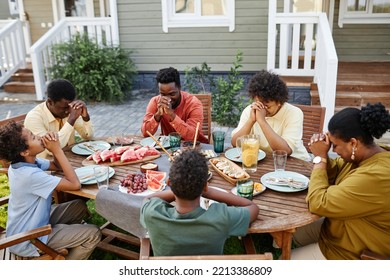 High Angle View At Group Of African American People Praying At Picnic Table Outdoors During Family Gathering