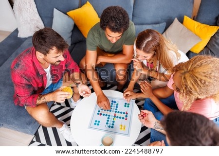 High angle view of group of cheerful young friends having fun playing ludo board game while spending time together at home