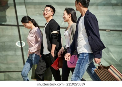 high angle view of group of four young asian people chatting talking conversing while walking on street with shopping bags in hands